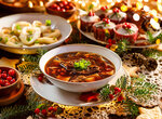 Schale mit dunkler Suppe, garniert mit Petersilie, umgeben von weihnachtlicher Dekoration und weiteren Tellern mit Gebäck und Beilagen